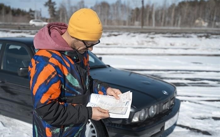 Мужчина изучает бумаги, находясь рядом с автомобилем марки BMW.