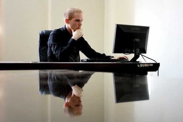 Чтобы выяснить информацию о своем страховом стаже, мужчина пребывает за столом и направляет глаза на экран компьютера.