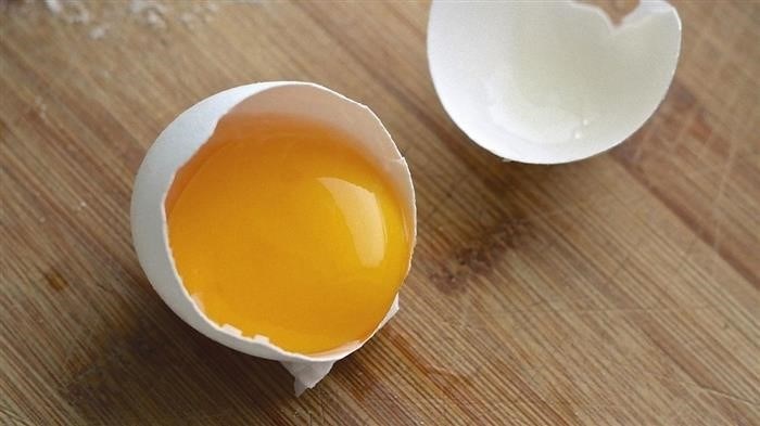 На столе лежат две разбитые половинки яйца. В одной из них остался белок вместе с желтком.